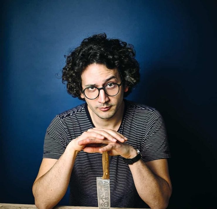 Alexis Ainouz sitting at a table with a chef's knife