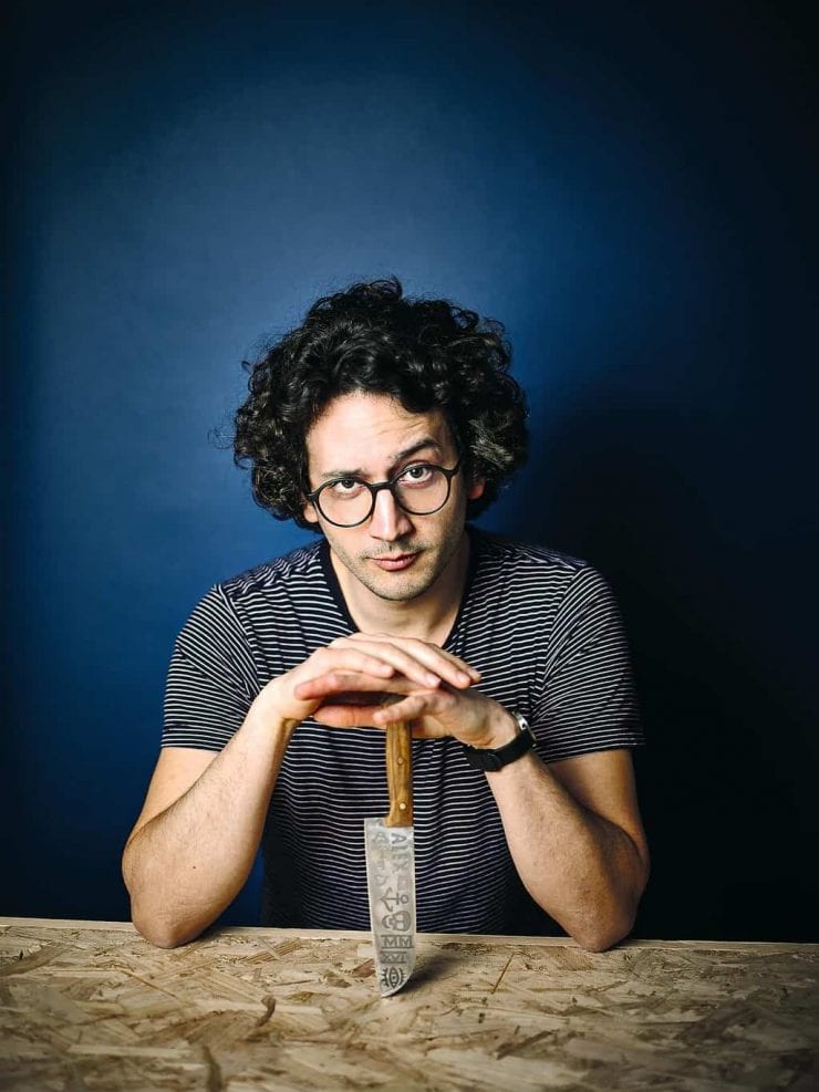 Alexis Ainouz sitting at a table with a chef's knife