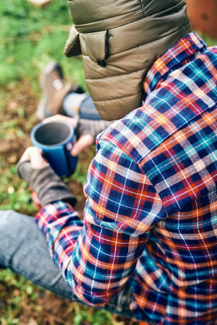 A man sits in the woods drinking coffee