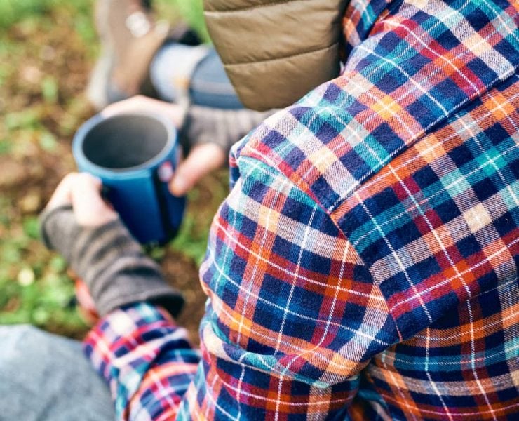 A man sits in the woods drinking coffee
