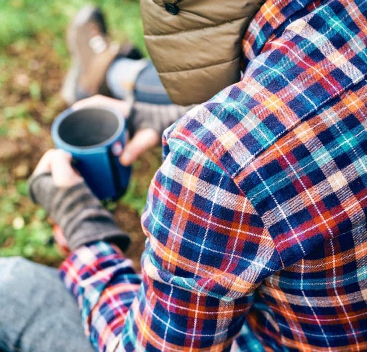 A man sits in the woods drinking coffee