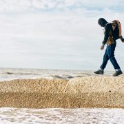 A man walks along a groyne on the beach