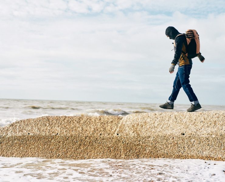 A man walks along a groyne on the beach
