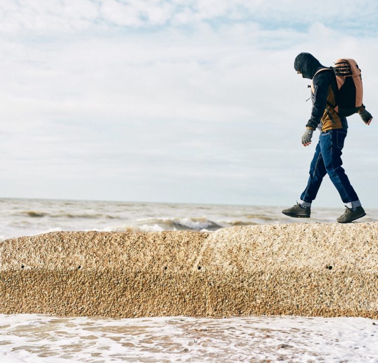 A man walks along a groyne on the beach