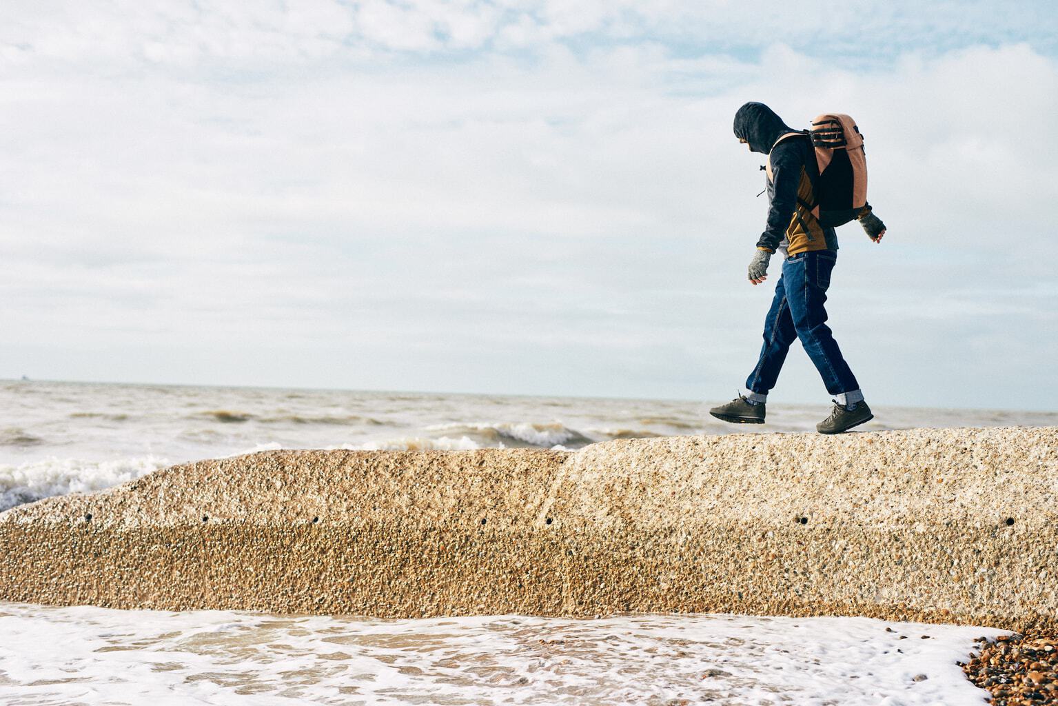 A man walks along a groyne on the beach