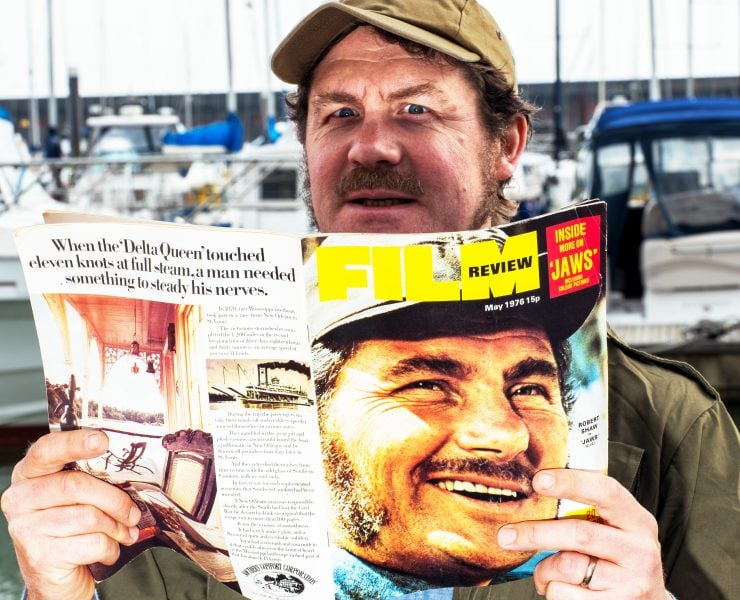Ian Shaw dressed as Quint reading a film magazine with his father's face on the cover