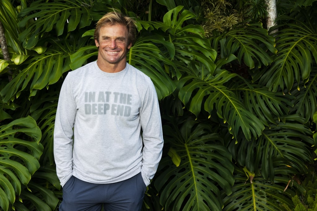 Laird Hamilton looking at a camera wearing a grey sweater with 'In at the deep end' written on it