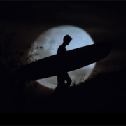 A man walking with a surfboard in the moonlight