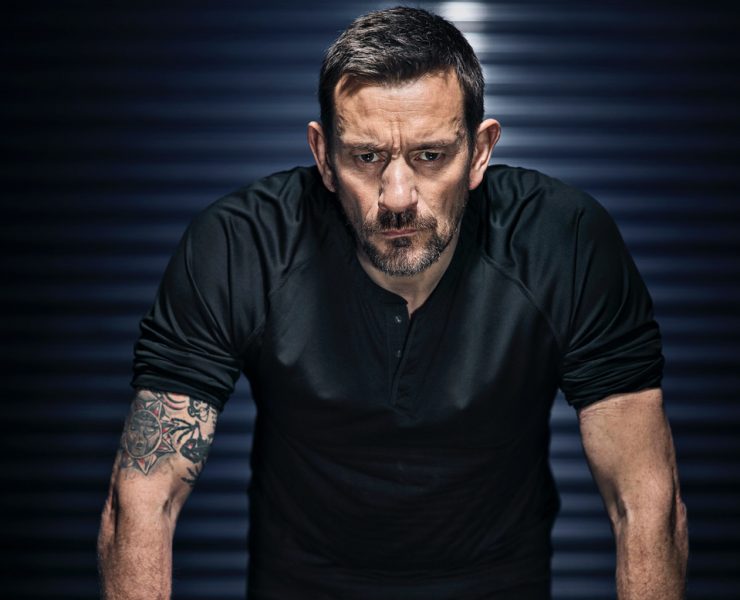 Ollie Ollerton stands with his hands on a desk