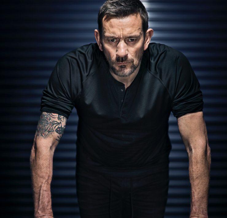 Ollie Ollerton stands with his hands on a desk