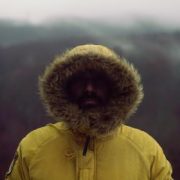 A man standing in the mountains with a fur hood covering his face
