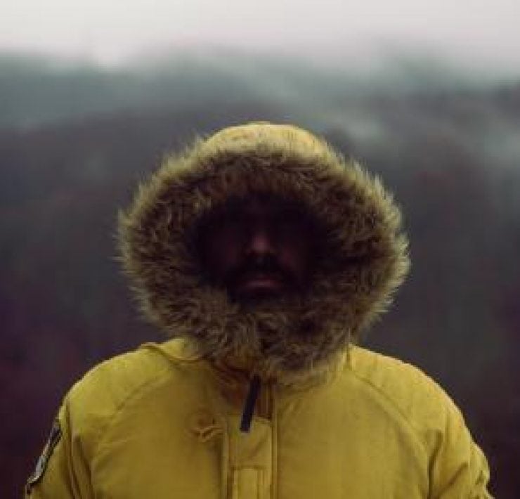 A man standing in the mountains with a fur hood covering his face