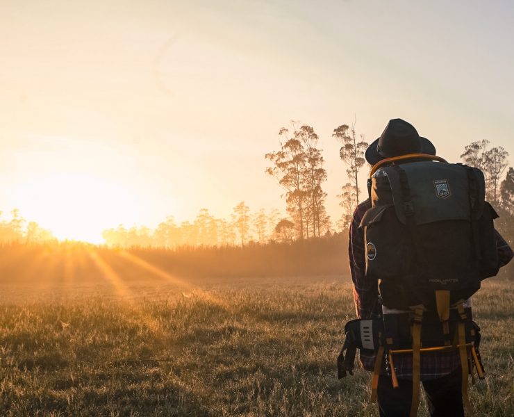 A man carrying a backpack observes the sunrise