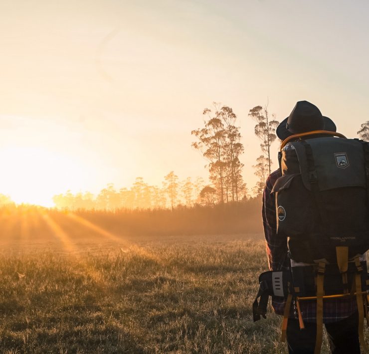 A man carrying a backpack observes the sunrise