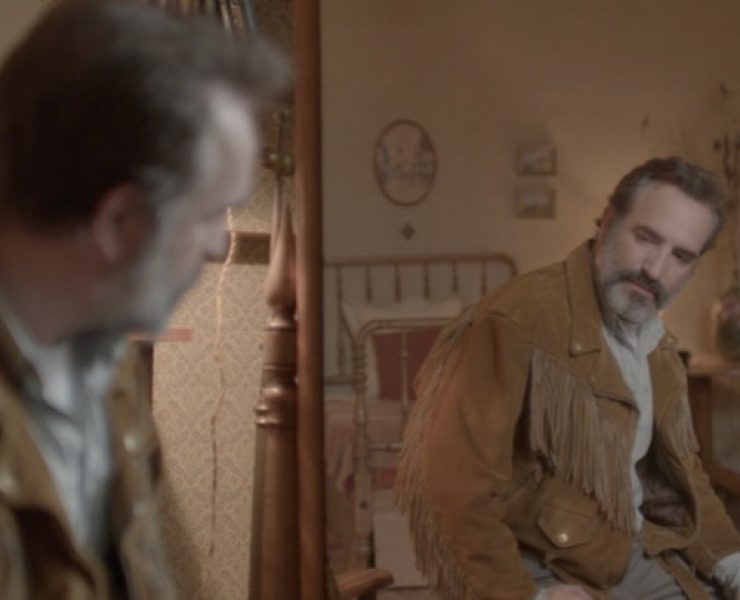 Jean Dujardin looks in a mirror at himself from a scene from Deerskin