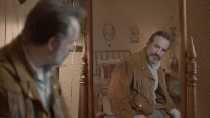 Jean Dujardin looks in a mirror at himself from a scene from Deerskin