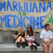 Two girls and a man sit in front of a sign saying 'Marijuana is Medicine' at Vancouver Hemp Rally