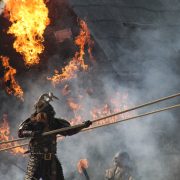A viking warrior holding a rope with fire behind him