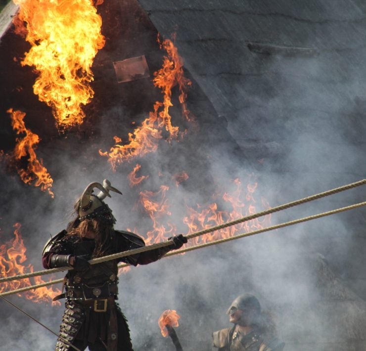 A viking warrior holding a rope with fire behind him